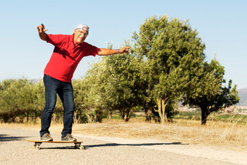 Anziano con maglia rossa  si diverte ad andare in skateboard in una strada di campagna  