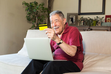 Anziano signore acquista con la propria carta di credito online da un computer portatile seduto nel proprio divano di casa