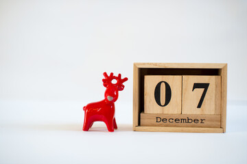 Cube wooden calendar showing date on 7th December with red ceramic reindeer figurine over white...
