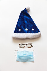 Christmas and New Year holidays in coronavirus pandemic. Blue Santa hat, goggles and a protective medical face mask to protect against the virus. Safe holidays concept. Flat lay, copy space, top view