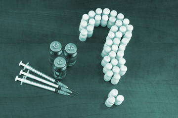 Many people shaped as question mark, vaccine bottles and syringes on wooden background. Questions...