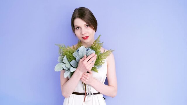 Girl with a bouquet isolated on a purple background. Girl with red lips hugs a bouquet of flowers. Girl hugs flowers. 