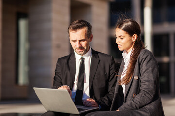 Middle aged mentor explaining presentation on laptop to young businesswoman sitting on bench...