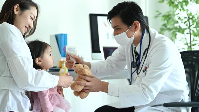 おもちゃであやしながら赤ちゃんの体温を測る医師