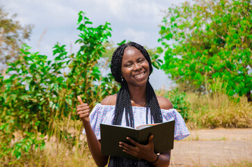 Fototapeta premium a young beautiful african school student feeling excited as she is going through her notebook and did thumbs up