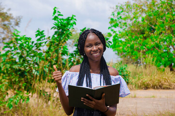 Fototapeta premium a young beautiful african school student feeling excited as she is going through her notebook and did thumbs up