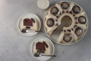Puding cookies. Two slices of black cookies pudding on white plate with a cup of milk and round big pudding at other corner in flat lay.