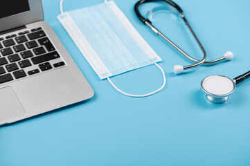 Doctor's Desk, laptop medical mask and stethoscope on blue background angle view