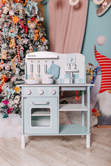 Christmas gifts for kids under the tree. Toy kitchen present for girls. Christmas present under the tree. Toy wooden kitchen and dishes.
