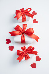 Gift boxes with red ribbon and hearts on white background. Valentines day background. Top view, flat lay. Vertical.