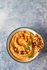 Bowl with homemade hummus garnished with boiled chickpeas, seeds, flatbread and olive oil, blue concrete background. Top view.