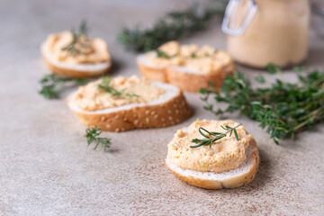 Homemade pate, spread or mousse in glass jar with sliced bread and herbs, light concrete background.