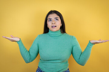 Young caucasian woman over isolated yellow background clueless and confused expression with arms and hands raised