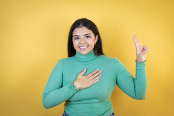 Young caucasian woman over isolated yellow background smiling swearing with hand on chest and...