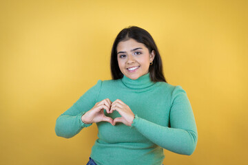 Young caucasian woman over isolated yellow background smiling in love showing heart symbol and shape with hands