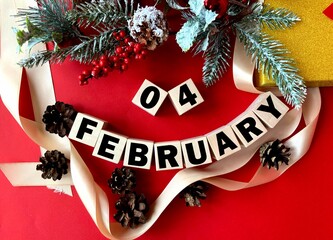 February 4 on wooden cubes.Near fir branches, cones, ribbon on a red background.Last month of...