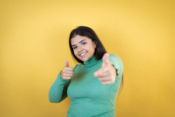 Young caucasian woman over isolated yellow background pointing to you and the camera with fingers, smiling positive and cheerful