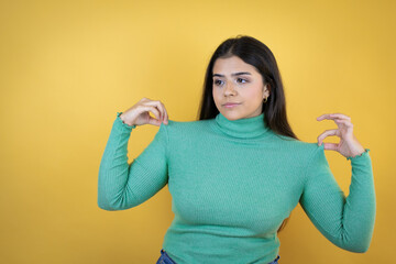 Young caucasian woman over isolated yellow background holding her t-shirt with a successful expression