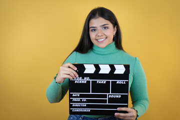 Young caucasian woman over isolated yellow background holding clapperboard very happy having fun