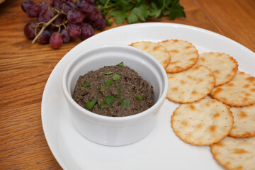 A dish of tapenade served on a white dish with crackers, grapes and parsley