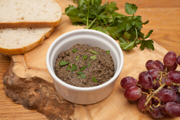A dish of tapenade with fresh herbs, grapes and sourdough served on a wooden platter