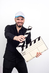 young man with a clapperboard in his hand smiling and joyful gesturing, wearing modern cap on a white neutral background and black shirt