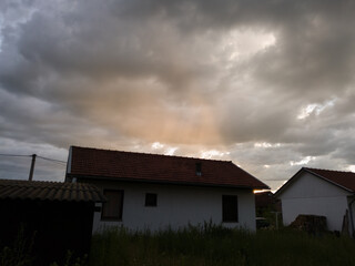 Storm overcast with dark clouds and rain and orange sun rays. Settlement with small houses and  unmowed lawns in Bosanski Brod, Bosnia and Herzegovina.