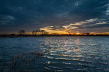 Fototapeta na wymiar Sunset and dark clouds over the lake with reeds