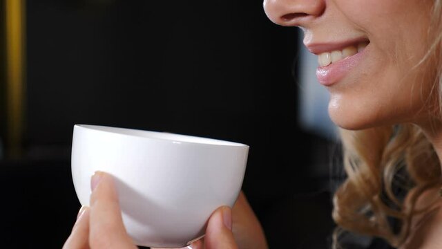 Portrait of relaxed girl having coffee break. Beautiful romantic girl with cup of coffee or tea enjoying. Cropped image of young smiling woman happy with coffee on dark background. 4 k video