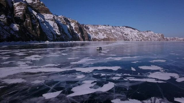 Flying of a drone over the ice of the lake behind a driving car along the rocky coast