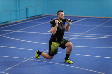 Fit sportsman in sportswear doing lunges with bulgarian bag in sport hall.