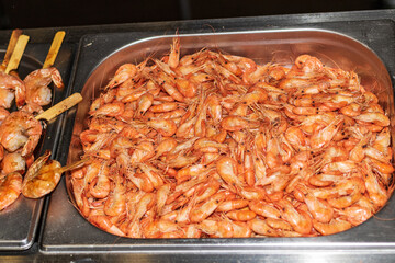 A large amount of freshly cooked shrimp is in a metal dish. Delicious food cooked over an open fire, which is offered at a street food fair, event, festival.