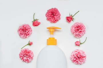 White plastic bottle with dispenser close-up with pink flowers and rosebuds on a white isolated background top view, close-up, skin care concept, hair Care, soap and balms, empty space for text