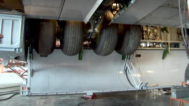 Chassis maintenance. Il-76 aircraft stands on hydraulic elevators. Close-up. Doors of chassis niche open. Landing gear move down. Niche doors of chassis are closed.