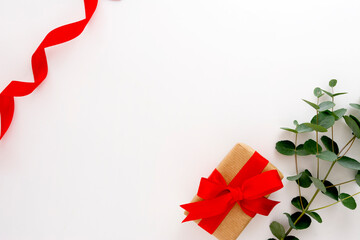 Gift box wrapped in brown paper decorated with eucalyptus branch and red bow on white, copy space.