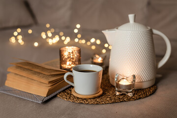 Still life teapot, book, cup of coffee, candles in the living room on a wooden table. Cozy interior concept