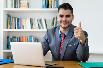 Laughing mexican businessman at computer showing thumb up at office