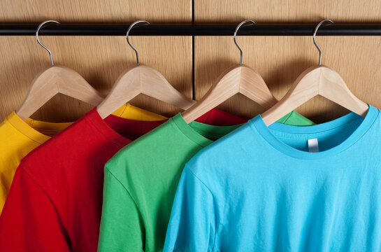 Four colorful t-shirts hanging outside a wardrobe. Studio photo.