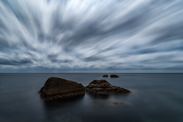 Minimalistic long exposure night seascape with motionless water, four rocks and moving clouds