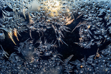 Beautiful crispy frost structure with frozen water drops on a window pane as a natural Christmas greeting card. Sun light and Orange flashes have got ice corners. Night Navy Blue Background.