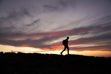 Silhouette of traveller with a backpack climbing up the mountain against beautiful horizon