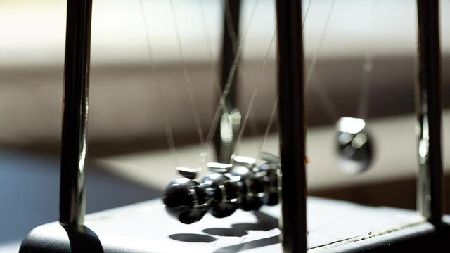 Hand putting the Newton's cradle in motion in sunlight, macro, extreme closeup. Metal balls swinging and slowing down. Moving something, inertia concept, science, fun physics lesson toy, real time