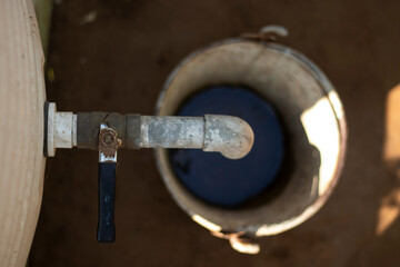 Close up of water tap, Bucket half filled with water