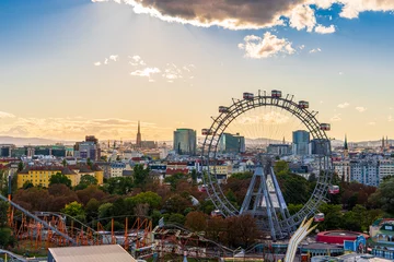 Fototapeten City view of Vienna, Austria, from above at Prater amusement park. Iconic fairy wheel and other amusement rides in the background with the sun peeking out of the clouds. © Uniqueton