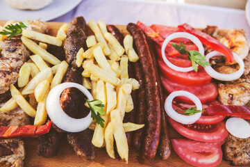 Tasty mixed grilled meat and french fries serving on wooden plate in the restaurant