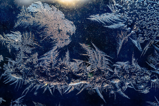 Ice patterns on glass on Christmas Eve. Sun lights and Orange flashes behaind the iced window. Night Navy Blue Background.