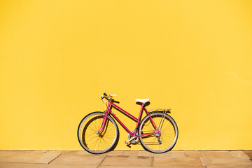 pink retro bike supported on a yellow wall
