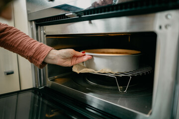 Woman putting in the oven a homemade cheesecake