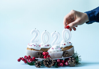 End of the year 2020 concept. Woman put out candles on cupcakes  on blue background. Copy space