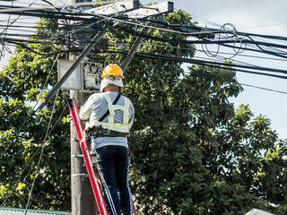 A technician on a ladder fixes a pole mounted fiber optic terminal splitter box to repair or...